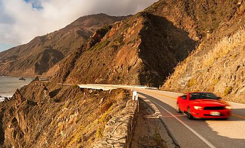 Photo of a red sports car driving along the California coast